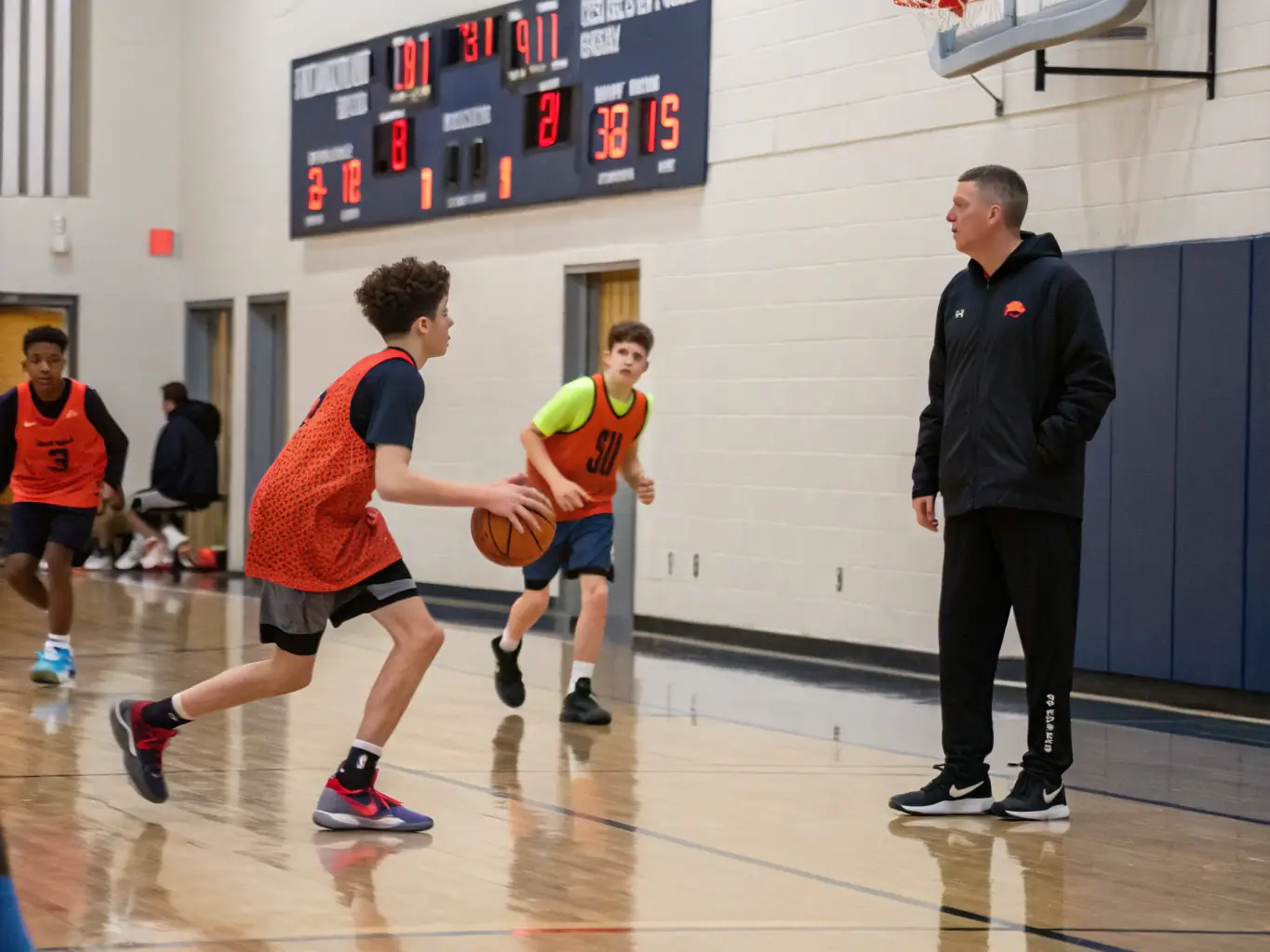 An action shot of teenagers engaged in a competitive basketball scrimmage, showcasing teamwork and strategic play, with coaches observing from the sidelines.